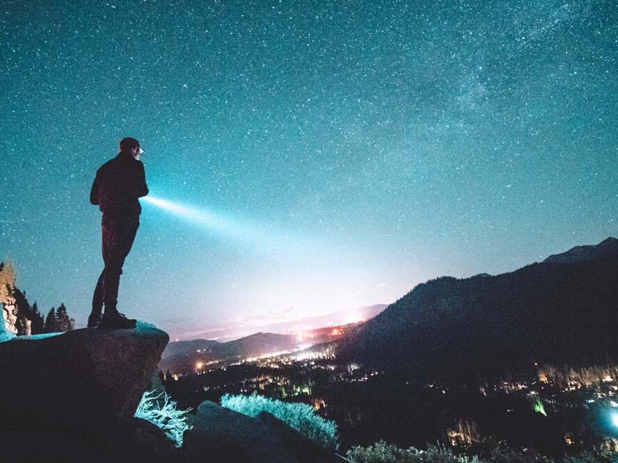 a man with a flashlight on a mountain under a starry sky