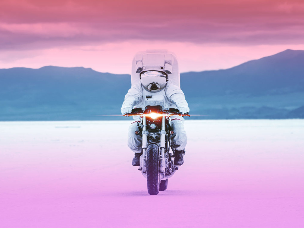 an astronaut on a motorcycle with mountains in the background