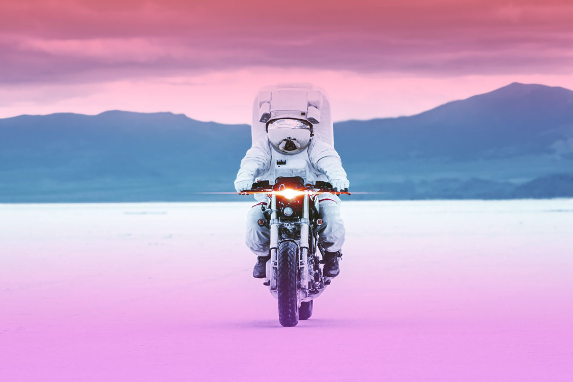 an astronaut on a motorcycle with mountains in the background