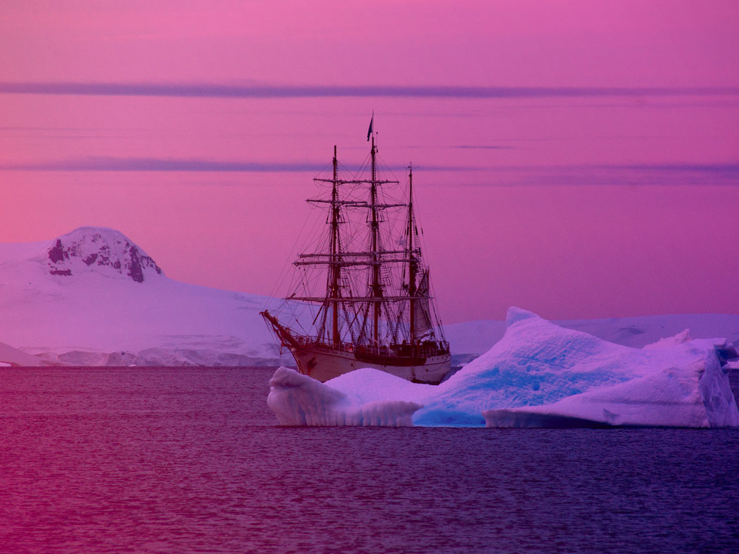 an old-fashioned ship sailing between icebergs at sunset