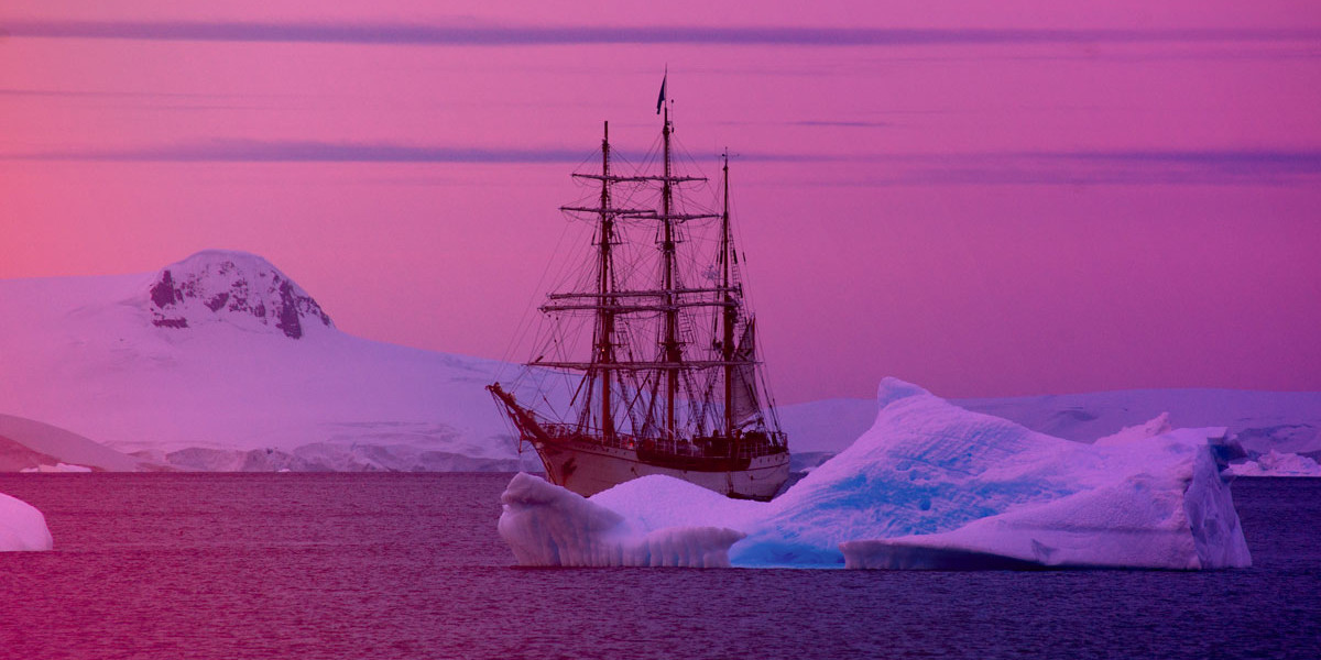 an old-fashioned ship sailing between icebergs at sunset