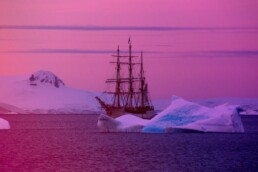 an old-fashioned ship sailing between icebergs at sunset