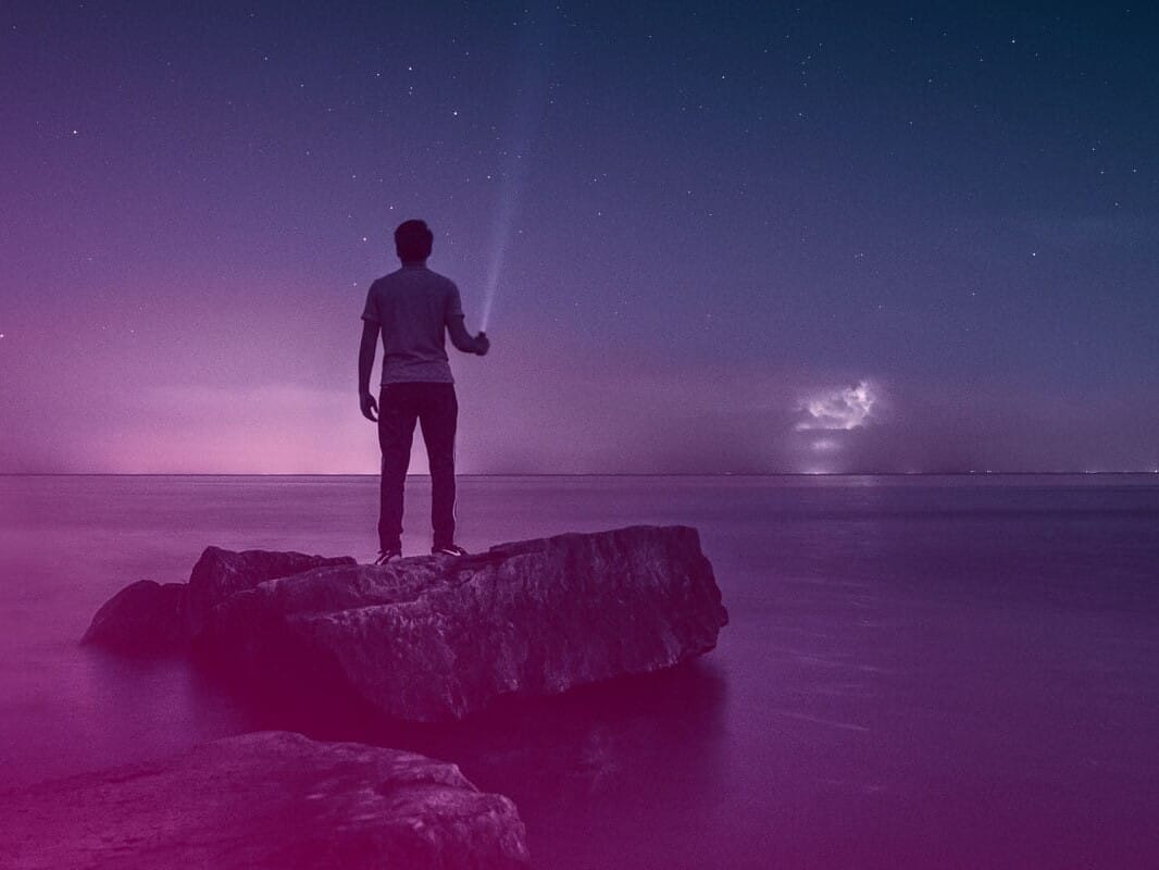 a man holding a flashlight standing on a rock overlooking the sea at dusk