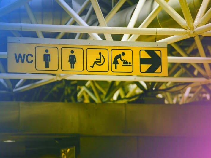 an accessibility sign in a subway station with icons for men, women, the disabled, mothers, and more with a blue and pink gradient overlaid on top.