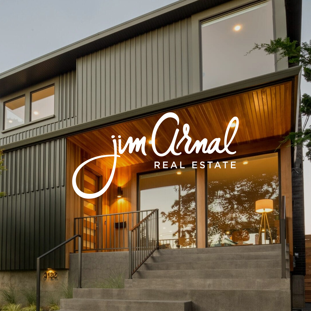 Modern two-story house with large windows, wood and metal exterior, steps leading to glass front door, and a lamp visible inside; Jim Arnal Real Estate logo prominently overlaid.